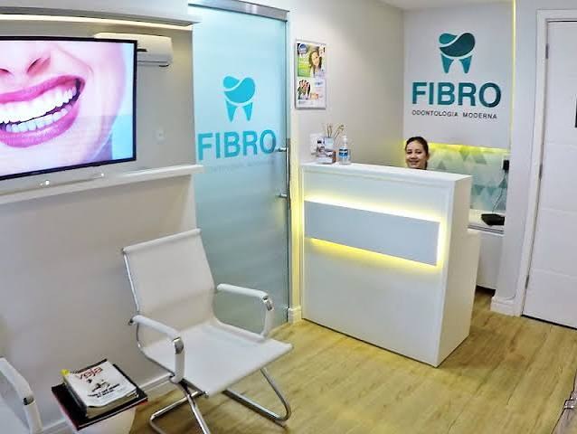 Recepção da Fibro Odontologia, com o logo na parede e balcão iluminado